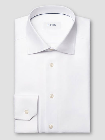 The Eton Slim Fit Solid Textured Twill Dress Shirt in White features a classic collar and single cuff, neatly folded with pearl buttons and displayed against a plain light gray background.
