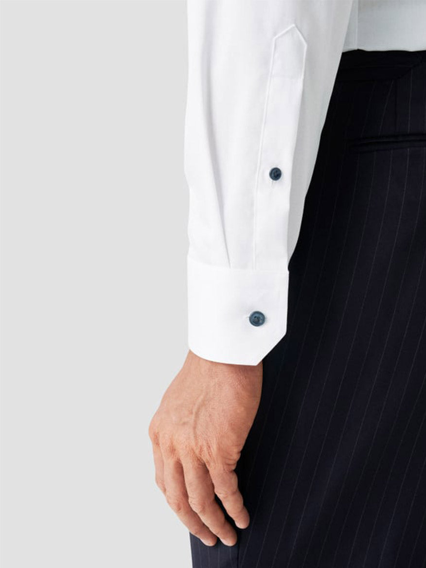 A person wears the Eton Contemporary Fit Solid Signature Twill Dress Shirt in White with Navy Details and black pinstriped trousers, shown from wrist to mid-thigh against a plain light background.