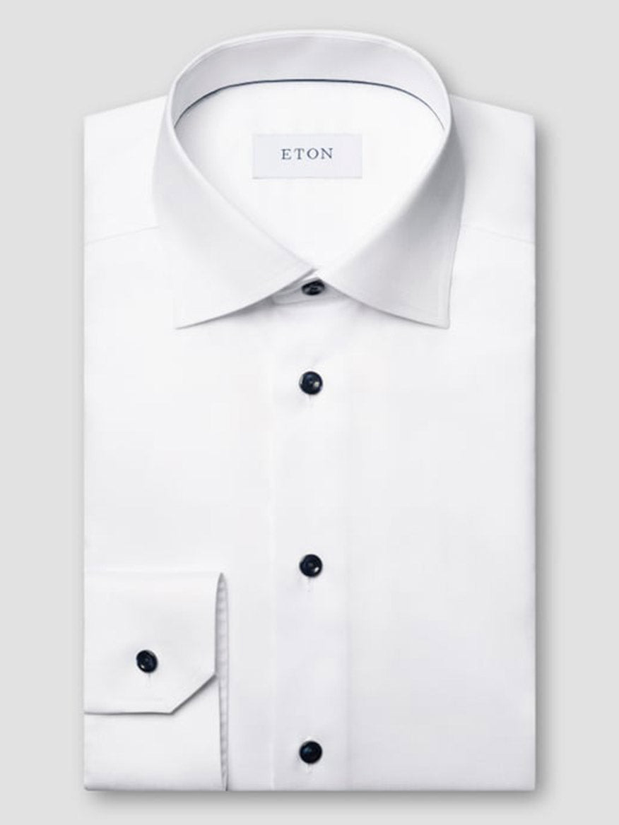 The Eton Contemporary Fit Solid Signature Twill Dress Shirt in white with navy details is neatly folded, showcasing its spread collar and navy buttons against a plain light grey background. The inner label reads "ETON.