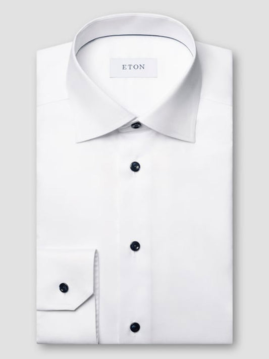 The Eton Contemporary Fit White Twill Dress Shirt with navy details is neatly folded, featuring a classic collar, black buttons, and an "ETON" label inside the collar, displayed against a plain gray background.