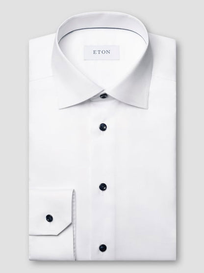 The Eton Slim Fit Solid Signature Twill Dress Shirt in white with navy details is neatly folded and displayed on a light gray background.