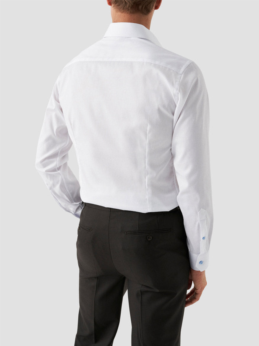A man wearing an Eton Contemporary Fit White Twill Dress Shirt With Blue Details and black dress pants, facing away from the camera against a plain light gray background.