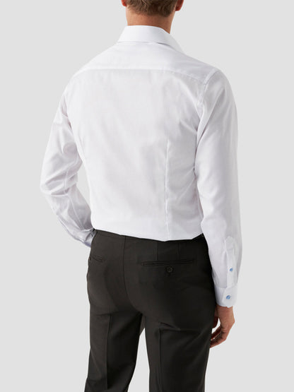A man wearing an Eton Contemporary Fit White Twill Dress Shirt With Blue Details and black dress pants, facing away from the camera against a plain light gray background.