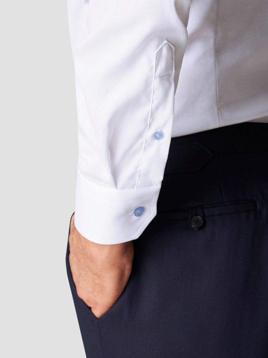 Wearing the Eton Contemporary Fit White Twill Dress Shirt With Blue Details and dark trousers, one hand in their pocket, a person perfectly embodies modern style.