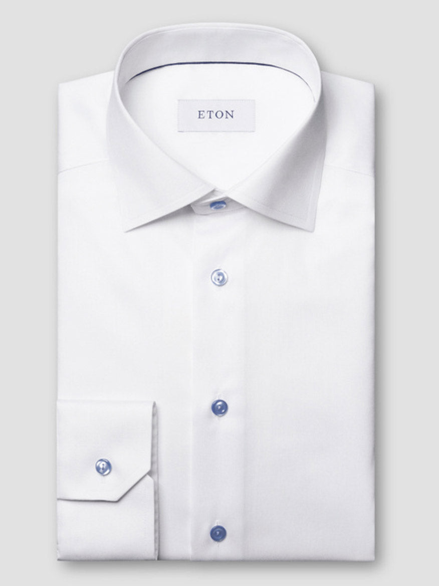 The Eton Contemporary Fit White Twill Dress Shirt with blue details features a spread collar and is neatly folded, displayed on a plain light gray background.