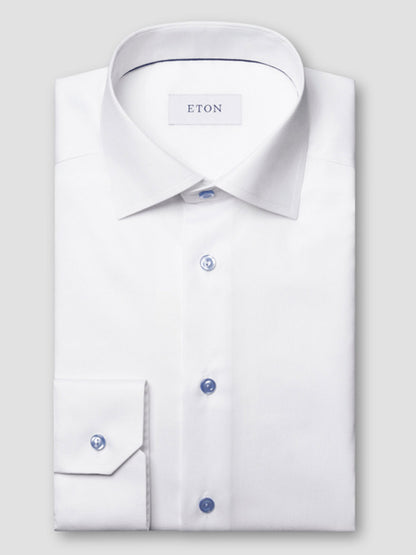 The Eton Contemporary Fit White Twill Dress Shirt with blue details features a spread collar and is neatly folded, displayed on a plain light gray background.