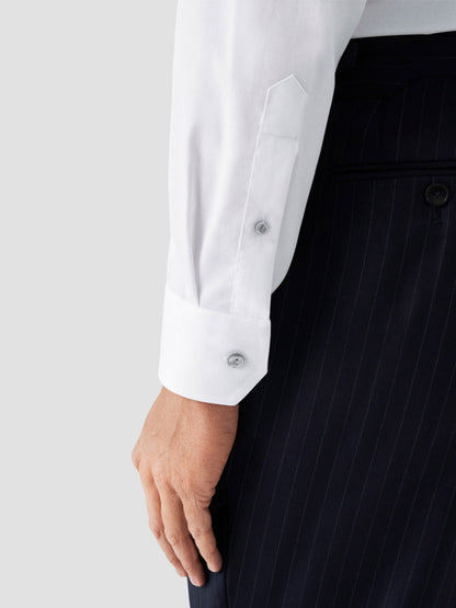 A person wearing an Eton Contemporary Fit White Twill Dress Shirt with grey details and dark pinstripe trousers, showing their hand by their side.