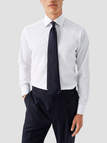 A man in an Eton Contemporary Fit White Twill Dress Shirt with grey details stands with one hand in his pocket against a plain background.