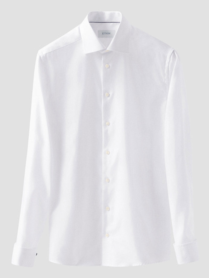 The Eton Slim Fit Solid Textured Twill Dress Shirt in White with French cuffs hangs against a light grey background, showcasing its crisp cut, long sleeves, and premium organic cotton fabric.