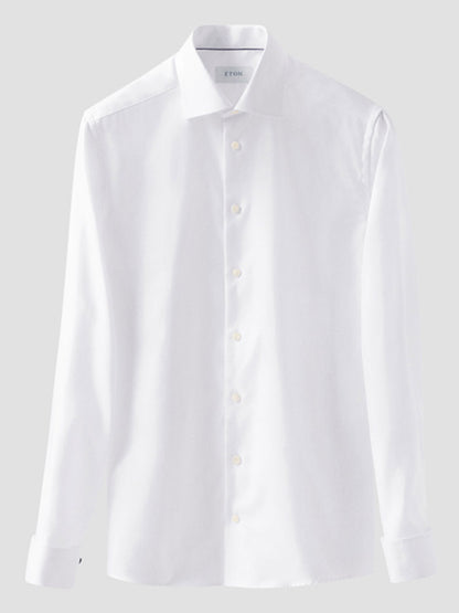 The Eton Slim Fit Solid Textured Twill Dress Shirt in White with French cuffs hangs against a light grey background, showcasing its crisp cut, long sleeves, and premium organic cotton fabric.