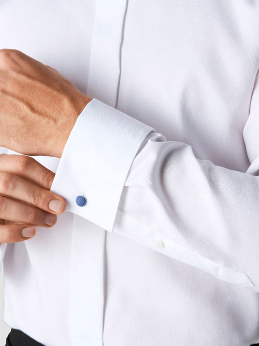 A person fastening the French cuffs of the Eton Contemporary Fit White Dobby Formal Shirt with a blue cufflink, ideal for black tie or formal evening wear.
