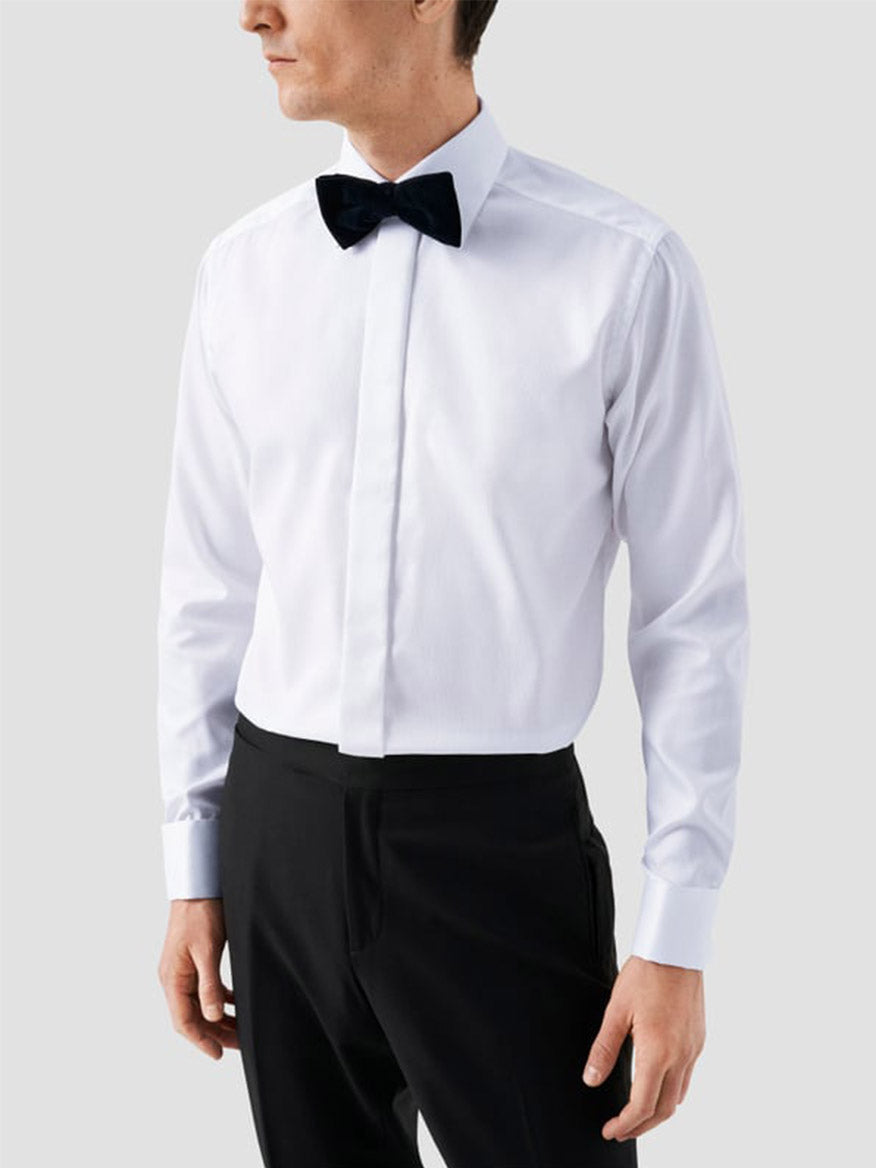 A man wearing an Eton Contemporary Fit White Dobby Formal Shirt with French cuffs, black bow tie, and black dress pants stands against a plain light grey background.