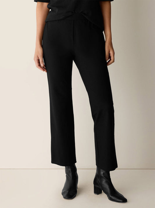 A person wearing Eileen Fisher Washable Stretch Crepe Kick Pants in black and black ankle boots, standing against a neutral background.
