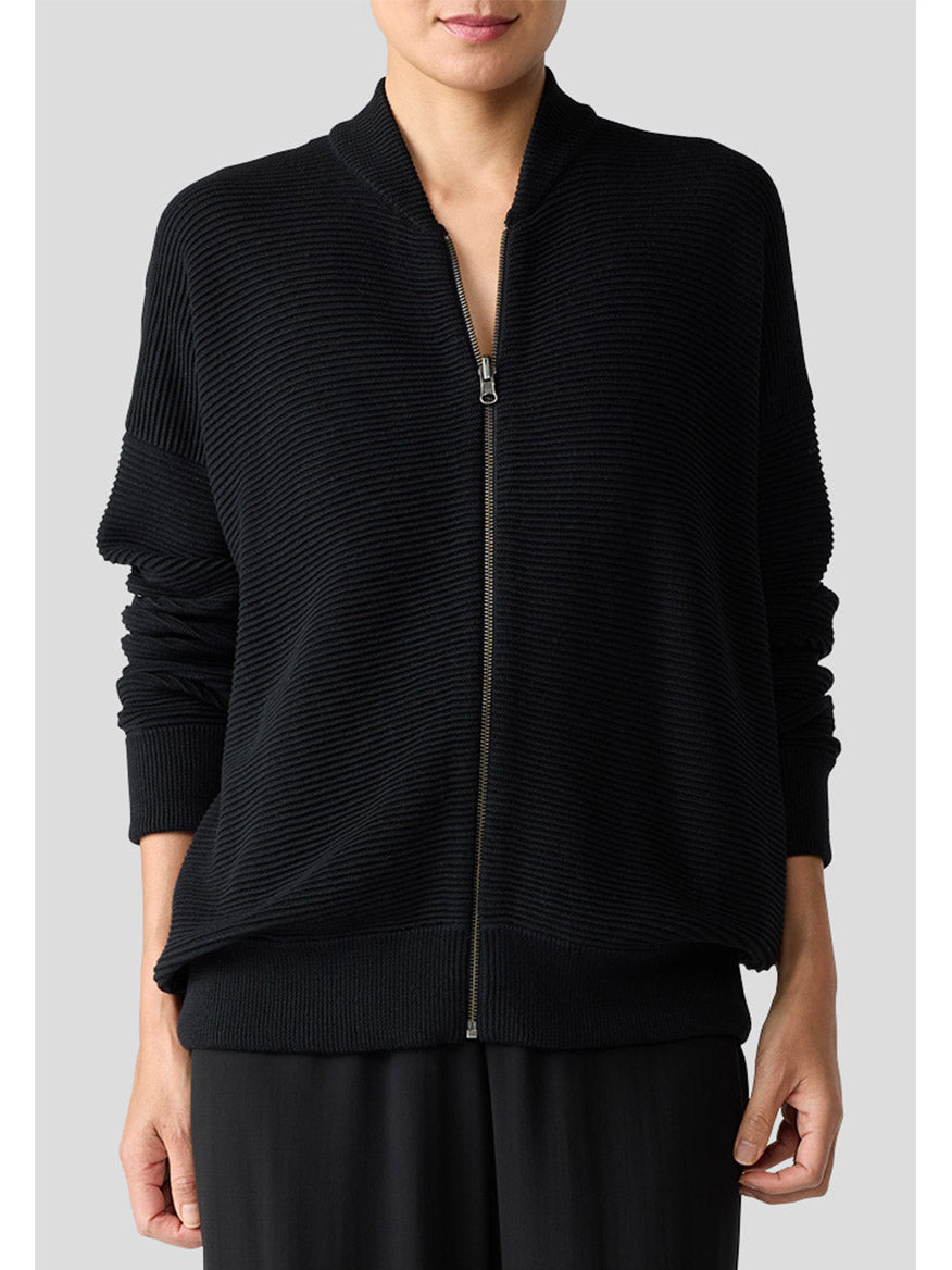 A person is wearing the Eileen Fisher Bomber Cardigan in black, paired with black pants against a plain background, highlighting a minimalist style with the cozy appeal of an organic-cotton blend.