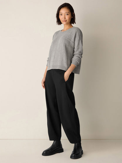 A person stands against a plain background wearing the Eileen Fisher Cotton & Recycled Cashmere Crew Neck Top in Dark Pearl, black wide-leg pants, and black ankle boots, with hands in pockets.