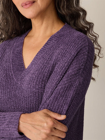 A woman with wavy hair wears the Eileen Fisher Chenille Blend V-Neck Top in Mulled Grape, featuring a boxy fit and textured finish, as she crosses her arms in front of a plain background.