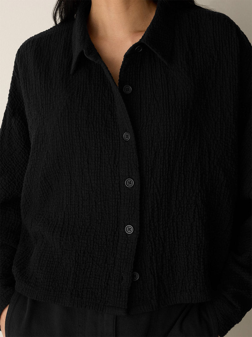 A person wears the Eileen Fisher Organic Cotton Doubleweave Classic Collar Jacket in Black, partially unbuttoned, paired with matching black boxy-fit pants. The image is cropped at the neck and waist.