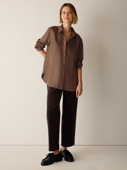 A person wearing an Eileen Fisher Silk Twill Classic Collar Shirt in Hazelwood with a classic collar, paired with dark brown trousers and black lace-up shoes.