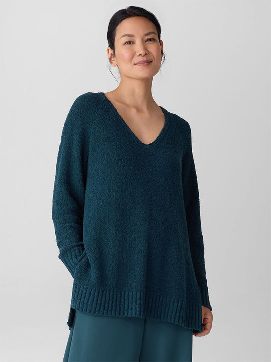 A woman stands against a plain background, wearing the Eileen Fisher Cotton Fluff V-Neck Top in Alpine paired with teal pants.