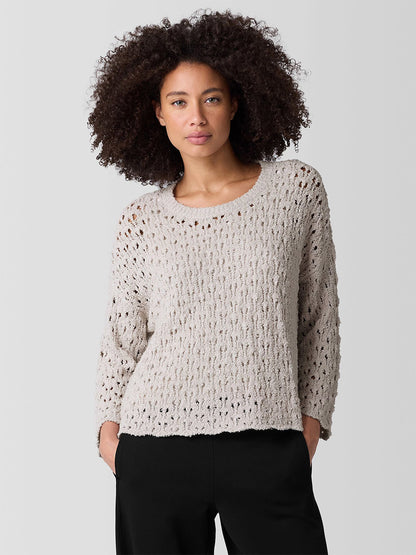 Someone with curly hair wears the Eileen Fisher Cotton Fluff Bracelet Sleeve Top in bone, a textured beige sweater with bracelet sleeves and a classic crew neck, paired with black pants against a plain background.