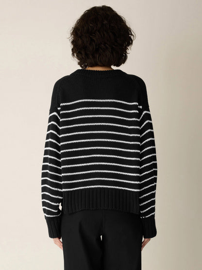A person with short curly hair is photographed from behind against a plain background, wearing the Eileen Fisher Peruvian Organic Cotton Cord Crew Neck Top in Black/White—a boxy-fit, striped top—paired with black pants.