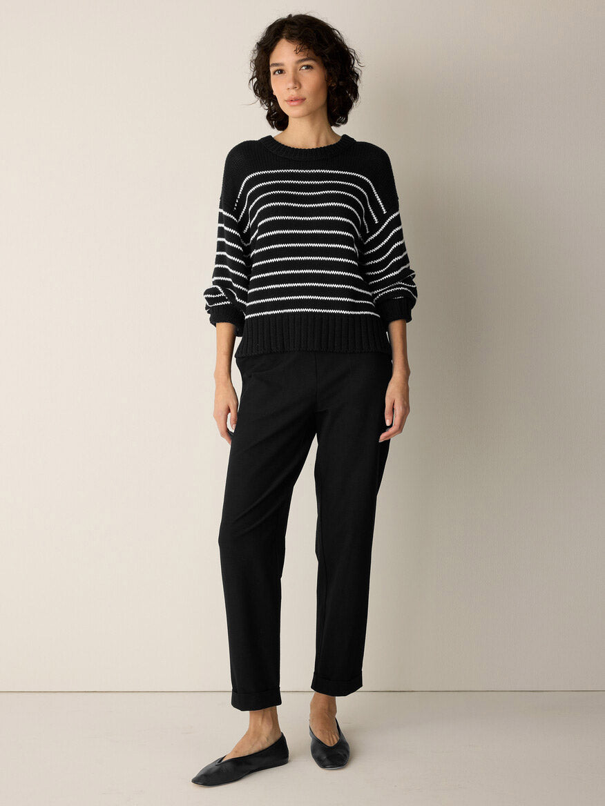 A person stands against a plain wall, wearing the Eileen Fisher Peruvian Organic Cotton Cord Crew Neck Top in Black/White, paired with black pants and black flats.