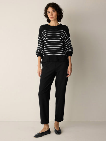 A person stands against a plain wall, wearing the Eileen Fisher Peruvian Organic Cotton Cord Crew Neck Top in Black/White, paired with black pants and black flats.