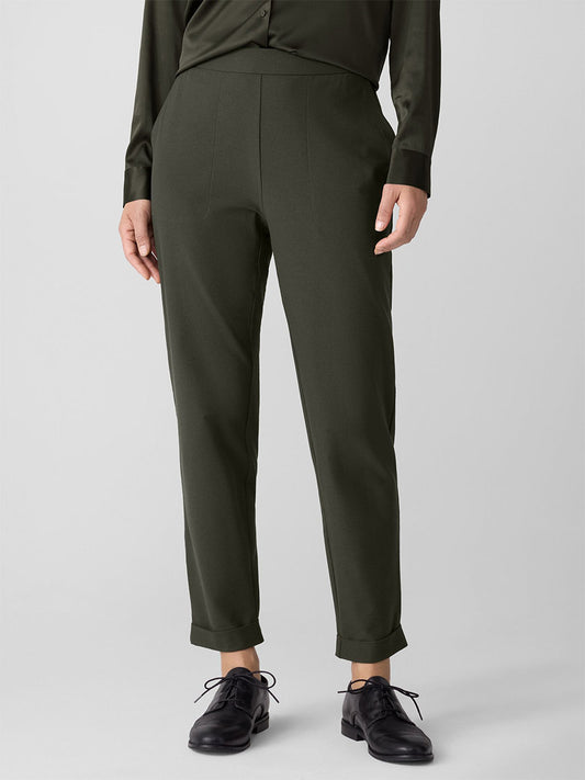 Person wearing Eileen Fisher Washable Stretch Crepe Cuffed Pant in Woodland, a dark green long-sleeve shirt, and black oxford shoes, standing against a plain light gray background.