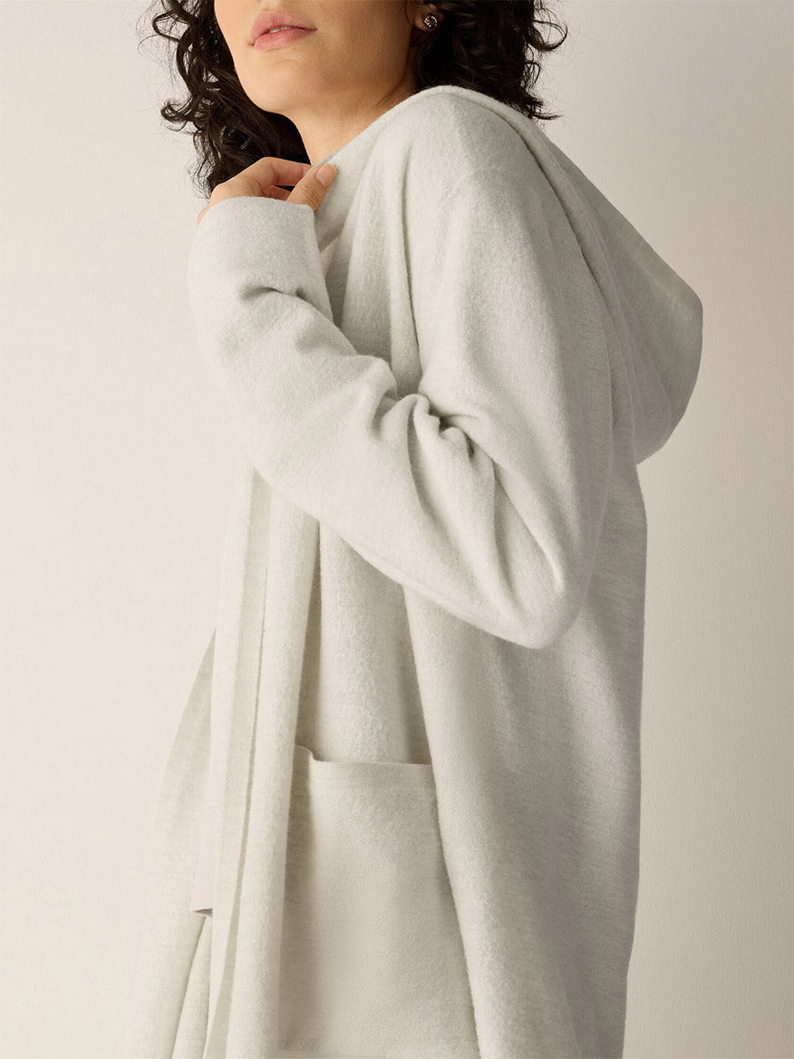 A person wearing an Eileen Fisher Fine Felted Wool Hooded Cardigan in Regenerative Wool in Plaster, a light gray fine wool hooded cardigan with front pockets.
