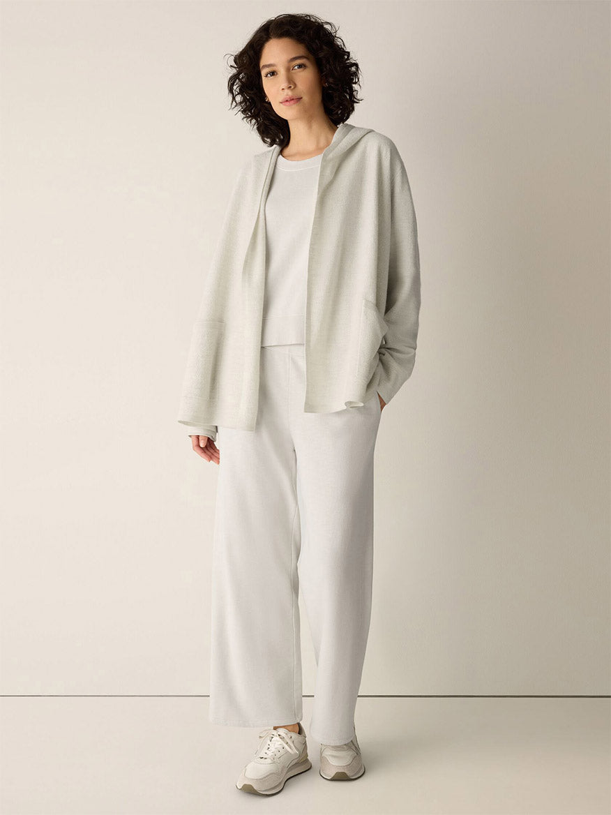 A person wearing an Eileen Fisher Fine Felted Wool Hooded Cardigan in Regenerative Wool in Plaster, a matching shirt, and wide-leg trousers with white sneakers.