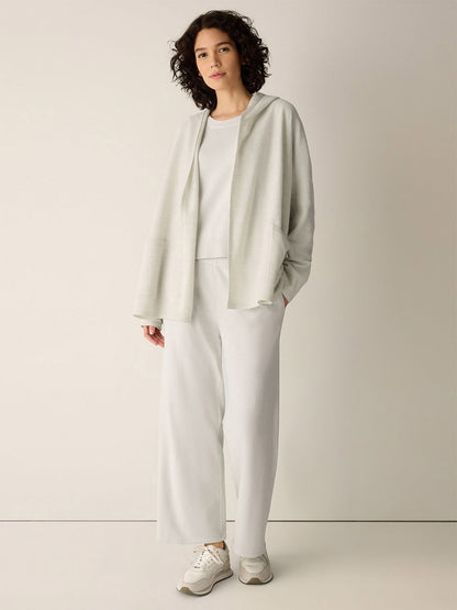 A person wearing an Eileen Fisher Fine Felted Wool Hooded Cardigan in Regenerative Wool in Plaster, a matching shirt, and wide-leg trousers with white sneakers.