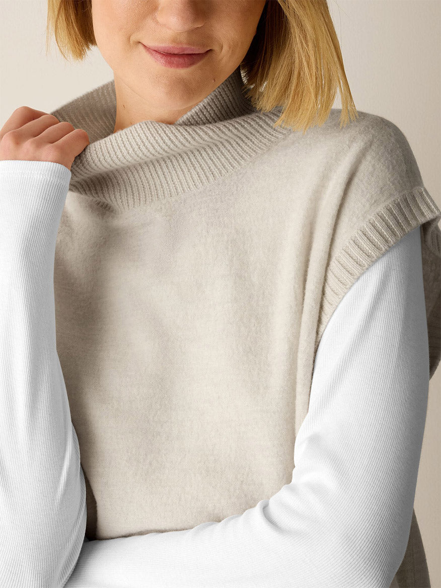 A person wears an Eileen Fisher Fine Felted Wool Turtleneck Top in Regenerative Wool in Plaster over a long-sleeved white shirt.