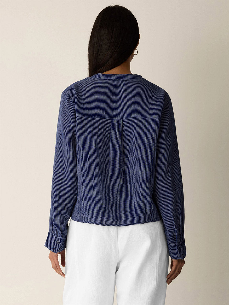 A person with long dark hair wears the Eileen Fisher Striped Organic Cotton Gauze Band Collar Shirt in Deep Dive, shown from the back against a plain background.