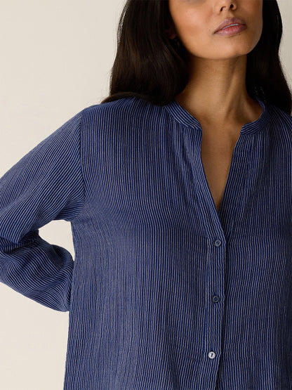 A person with long dark hair wears the Eileen Fisher Striped Organic Cotton Gauze Band Collar Shirt in Deep Dive.
