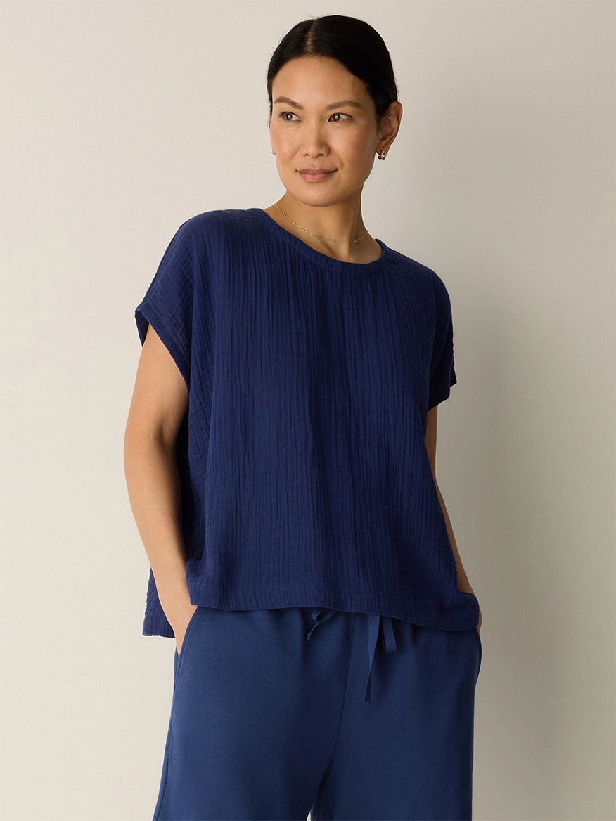 A woman stands against a plain background wearing the Eileen Fisher Organic Cotton Lofty Gauze Round Neck Box-Top in Deep Dive with matching navy blue pants, her hands in her pockets.