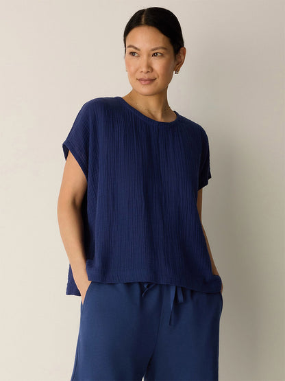 A woman stands against a plain background wearing the Eileen Fisher Organic Cotton Lofty Gauze Round Neck Box-Top in Deep Dive with matching navy blue pants, her hands in her pockets.