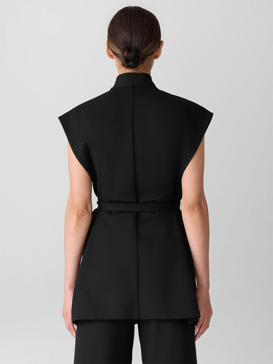 A person stands with their back to the camera, wearing the Eileen Fisher Washable Flex Ponte High Collar Vest in black and matching black pants, set against a plain light background.
