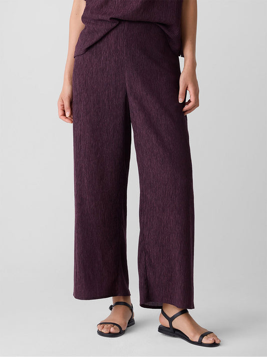 Model wears the Eileen Fisher Woven Plissé Wide-Leg Pant in Blackberry with a matching top and black flat sandals, ankle-baring, standing against a plain light gray background.