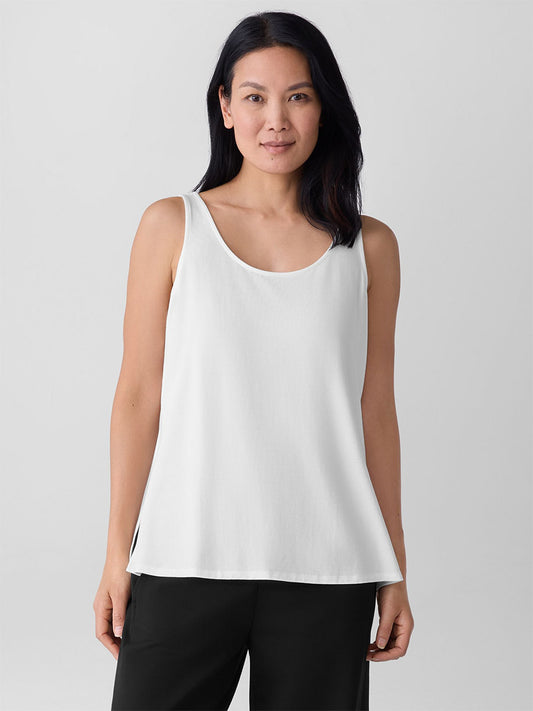 A person stands facing forward against a plain light background, wearing the Eileen Fisher Fine Jersey Scoop Neck Tank in White and black pants.