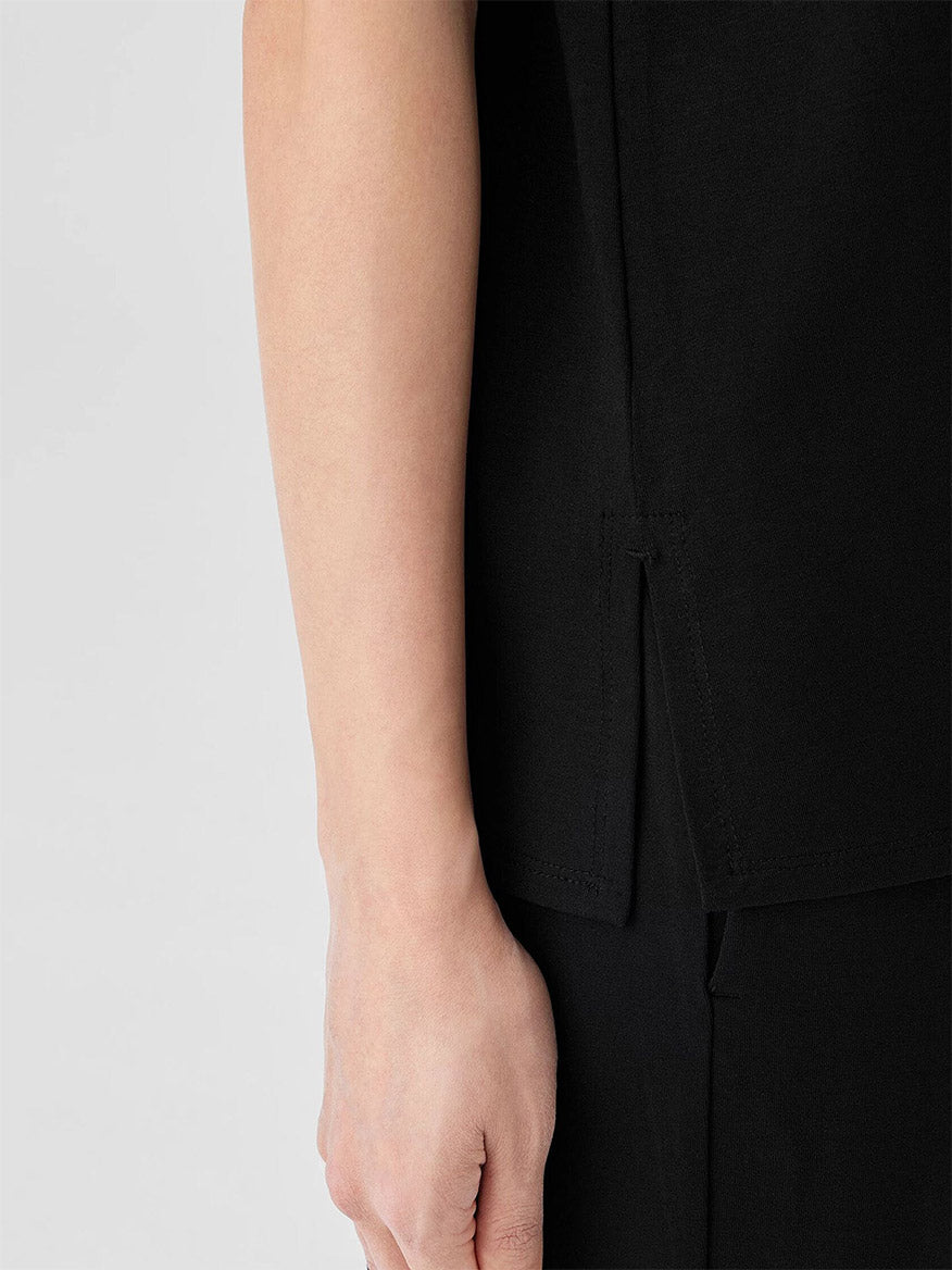 An individual's arm in the Eileen Fisher Stretch Jersey Knit Jewel Neck Shell in black, made from sustainable Tencel™ Lyocell with side slit detail, set against a plain gray background.