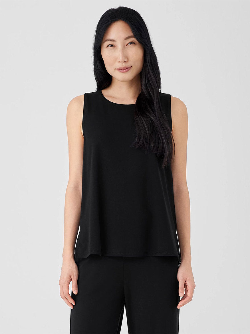 A person with long dark hair wears an Eileen Fisher Stretch Jersey Knit Jewel Neck Shell in black, standing against a plain light background.