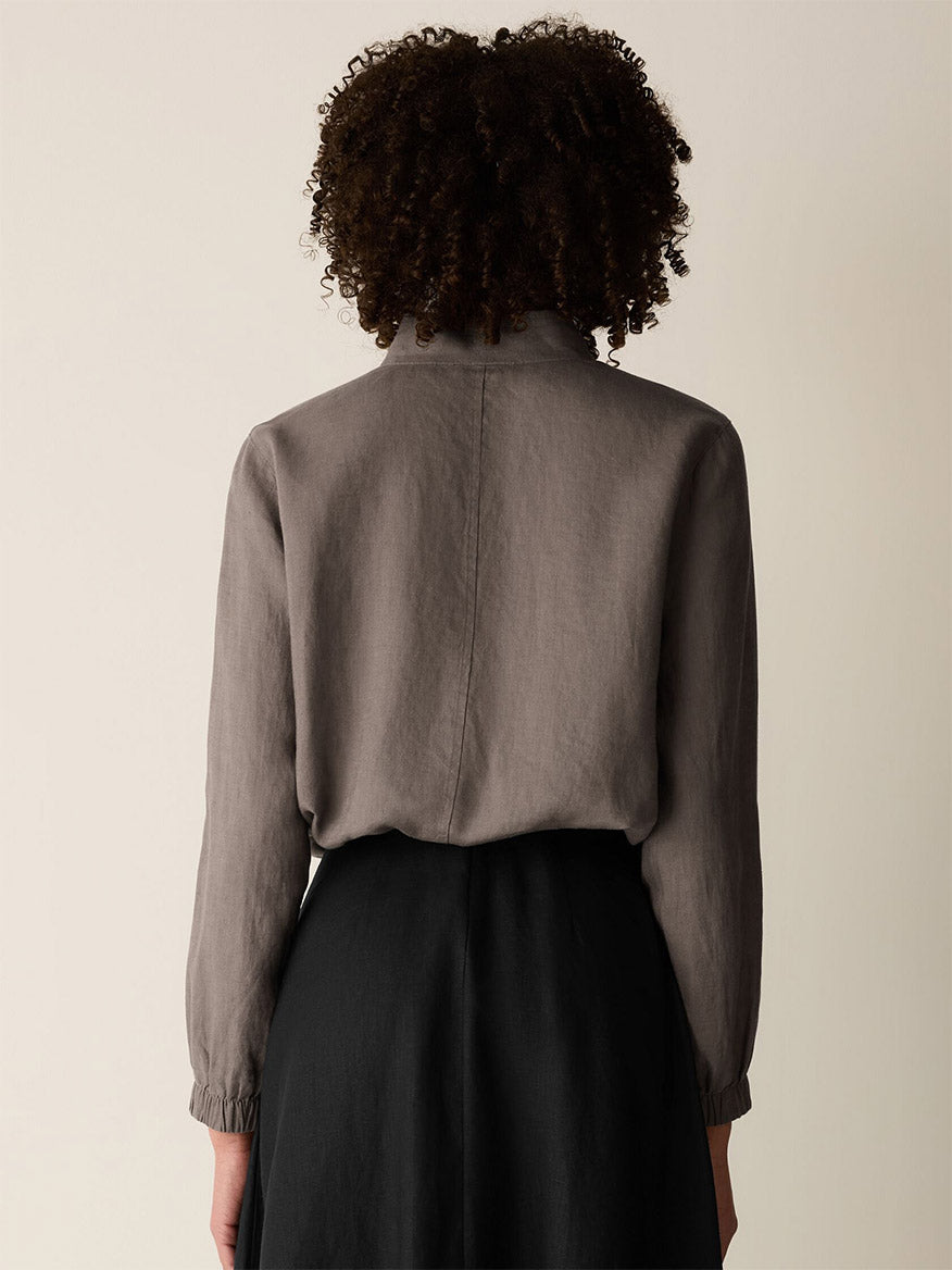 From the back, a person with curly hair wears the Eileen Fisher Organic Linen Flight Jacket in Walnut and a high-waisted black skirt, standing against a plain background.