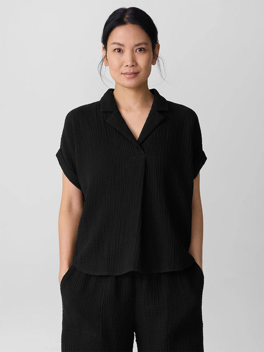 A person stands facing the camera, wearing the Eileen Fisher Organic Cotton Lofty Gauze Notch Collar Top in Black, paired with matching pants, against a plain light background.