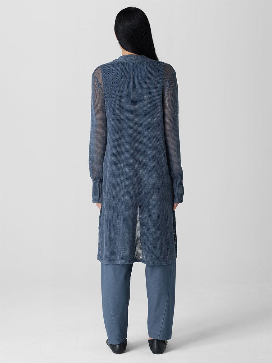 A person with long dark hair wears the Eileen Fisher Organic Linen Cotton Cord Long Cardigan in Eclipse over pants, standing with their back to the camera against a plain background.