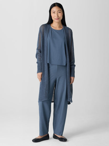 A person wears an Eileen Fisher Organic Linen Cotton Cord Long Cardigan in Eclipse, coupled with a chic top, pants, and black flats against a plain gray background.