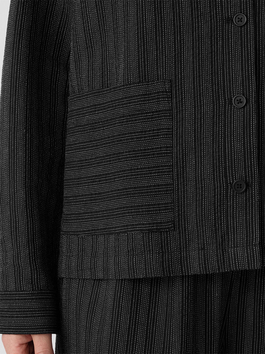 Close-up of the Eileen Fisher Cotton Blend Stripe Stitch Shirt Jacket in Black, showing thin white vertical stripes, a large patch pocket, buttons, and part of a person’s hand at the side.