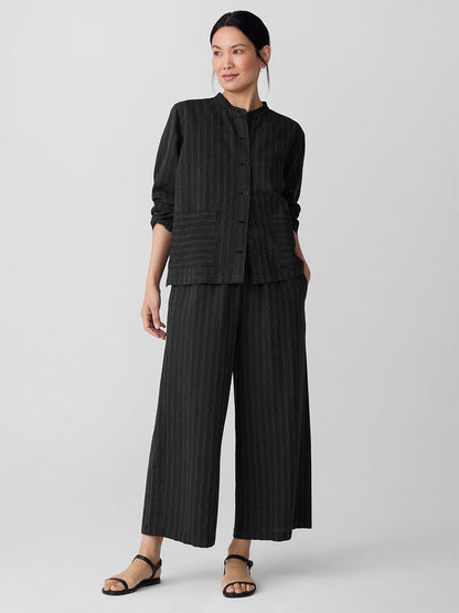 A woman stands against a plain background wearing the Eileen Fisher Cotton Blend Stripe Stitch Shirt Jacket in Black, styled with wide-leg pants and black sandals.