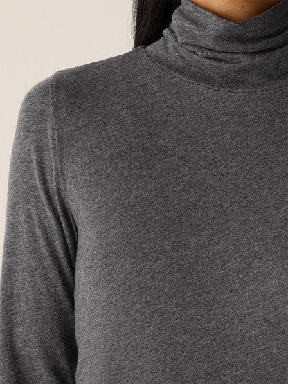 A close-up shows a person wearing the Eileen Fisher Mélange Sheer Cotton Blend Knit Turtleneck Top in Charcoal; only the lower face, neck, and upper torso are visible.