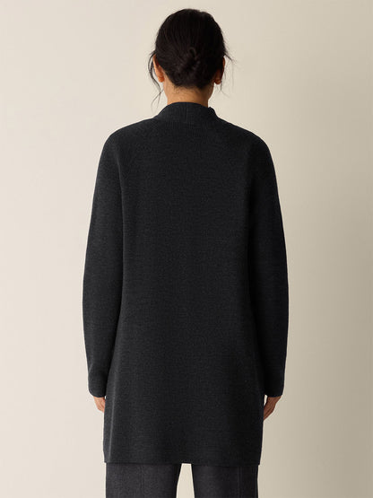 A person with dark hair in a low bun is shown from behind, wearing the Eileen Fisher Merino Long Cardigan in Charcoal and dark pants against a plain background.