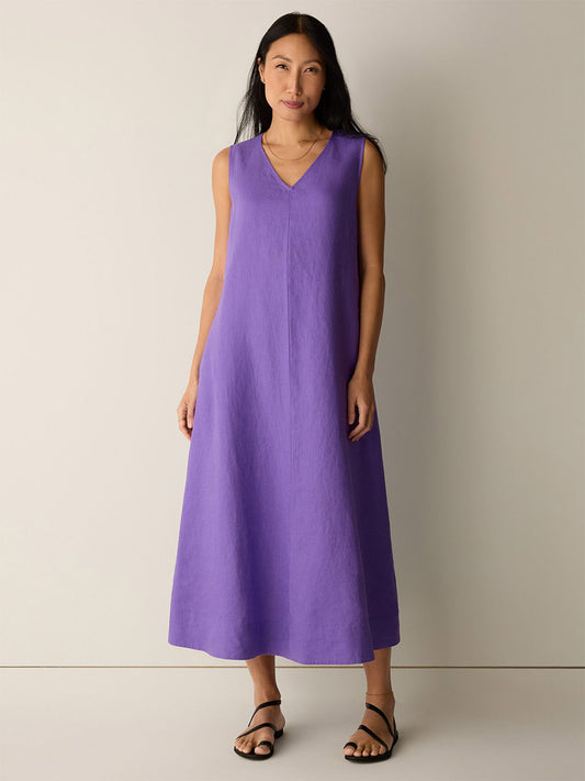 A woman stands against a plain background wearing the Eileen Fisher Organic Linen Easy Dress in Petunia and black sandals.